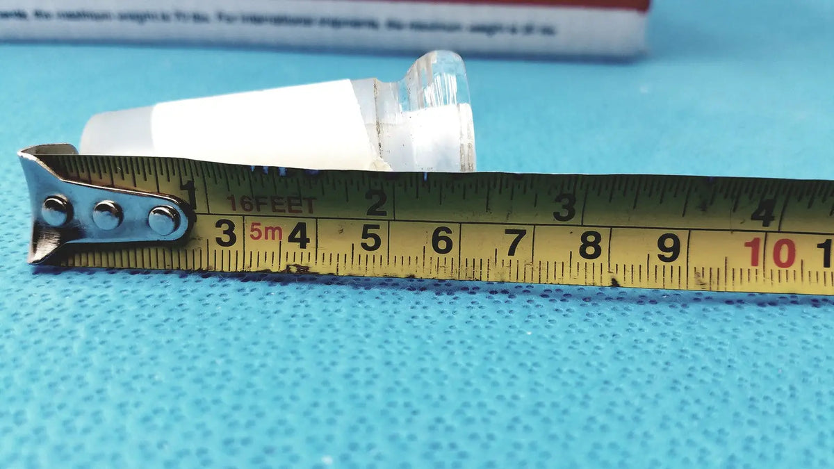 Yellow metal tape measure with black markings and silver hook alongside 24/40 lab glass adapter made of borosilicate glass