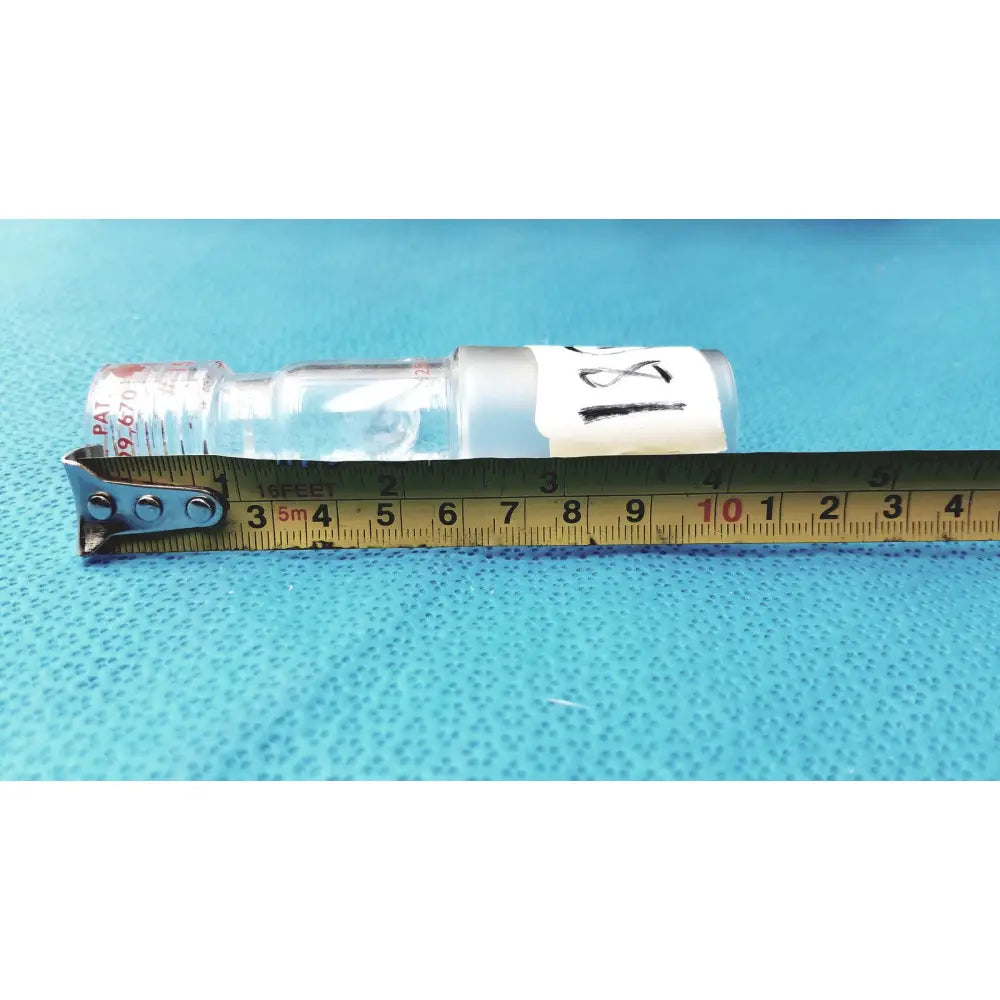 Clear glass ace glass chem-thread inlet adapter with white label and red cap text beside yellow measuring tape in laboratory glassware
