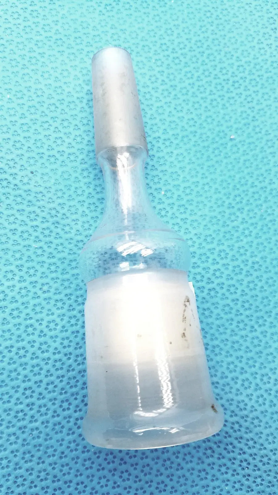 A translucent borosilicate glass ace glass enlarging adapter vial with frosted white cap and cloudy liquid inside