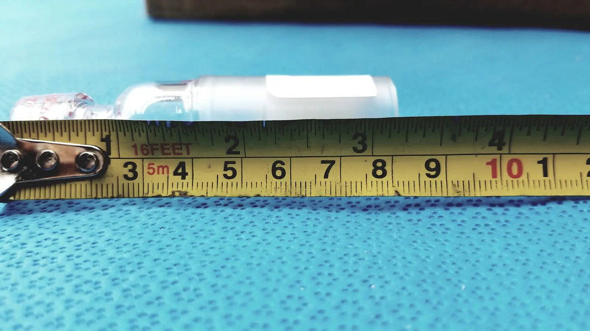A clear plastic ace glass thermometer adapter with a white cap on a blue surface next to a yellow measuring tape