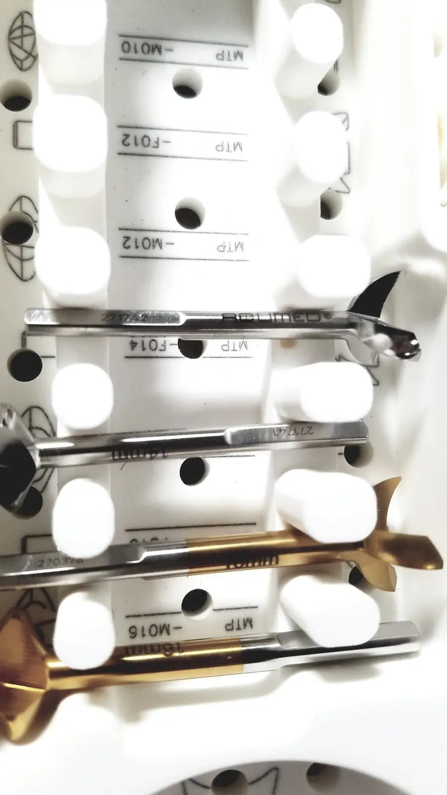 A set of metallic drill bits with black and gold tips in a white foam tray from acumed modular hand system set missing piece