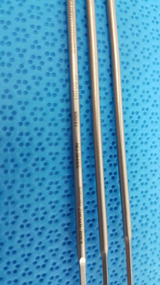 Three metallic aesculap laparoscopic instrument drill bits with engraved markings on a blue perforated surface