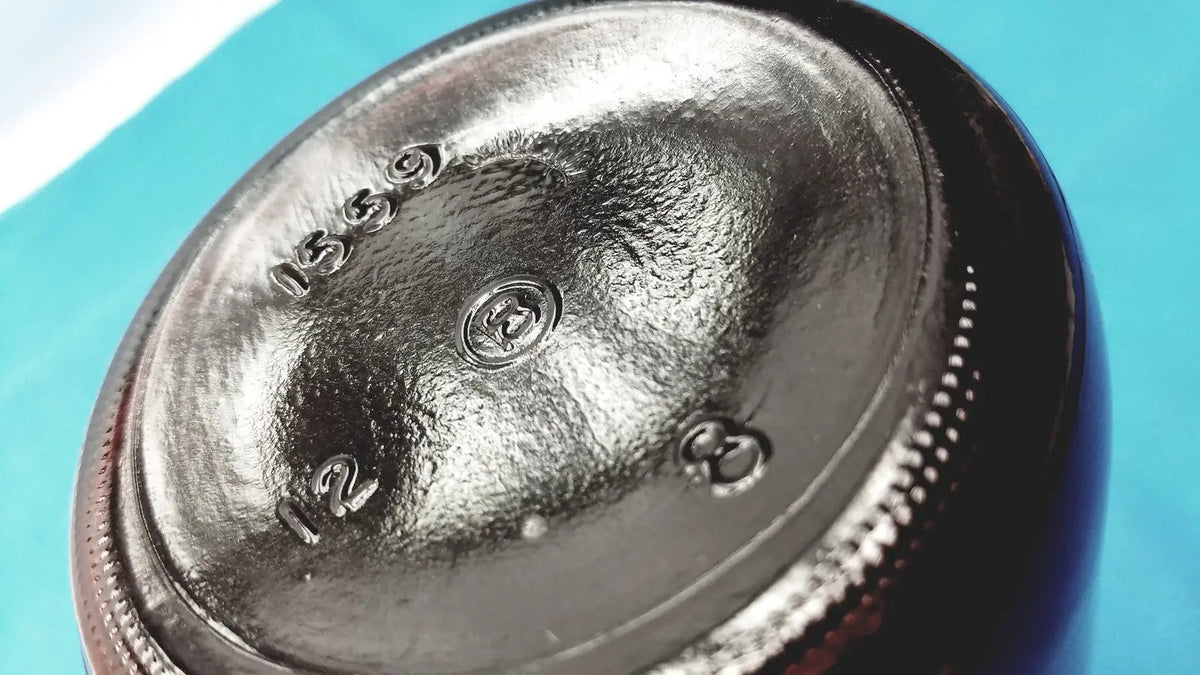 Bottom view of a dark glossy brown glass chemical bottle with embossed markings and circular logo for reagent storage lab use