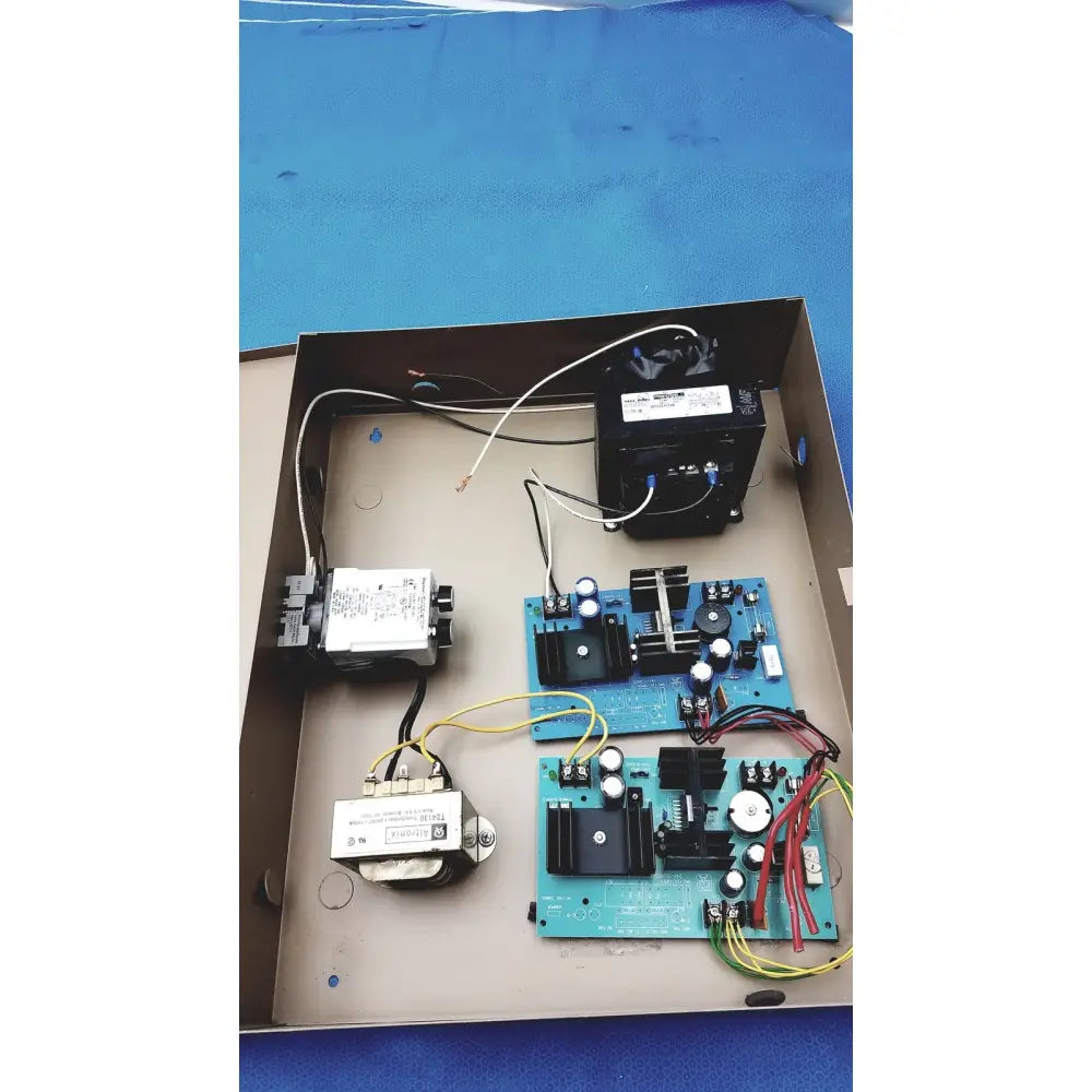 Blue circuit boards with black components and white capacitors inside a metal electrical control panel with time delay relay