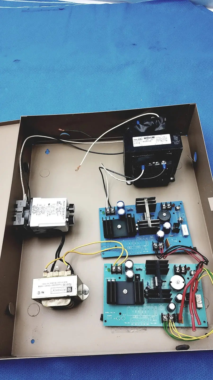 Blue circuit boards with black components and white capacitors inside a metal electrical control panel with time delay relay