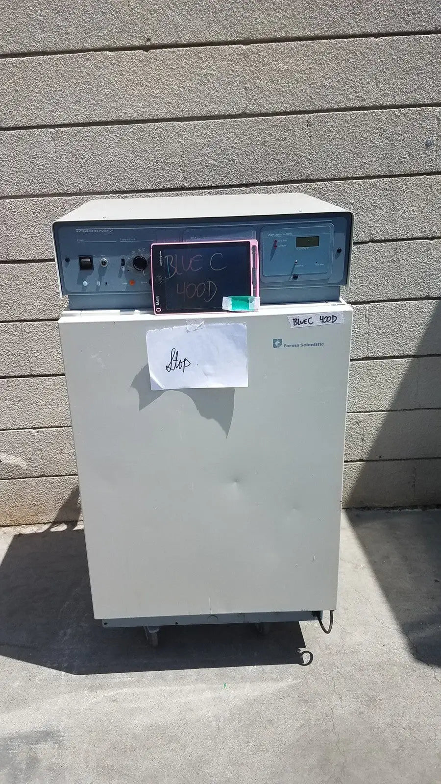 Gray laboratory freezer with blue control panel and chalkboard sign on top of forma scientific 3154 lab incubator for parts