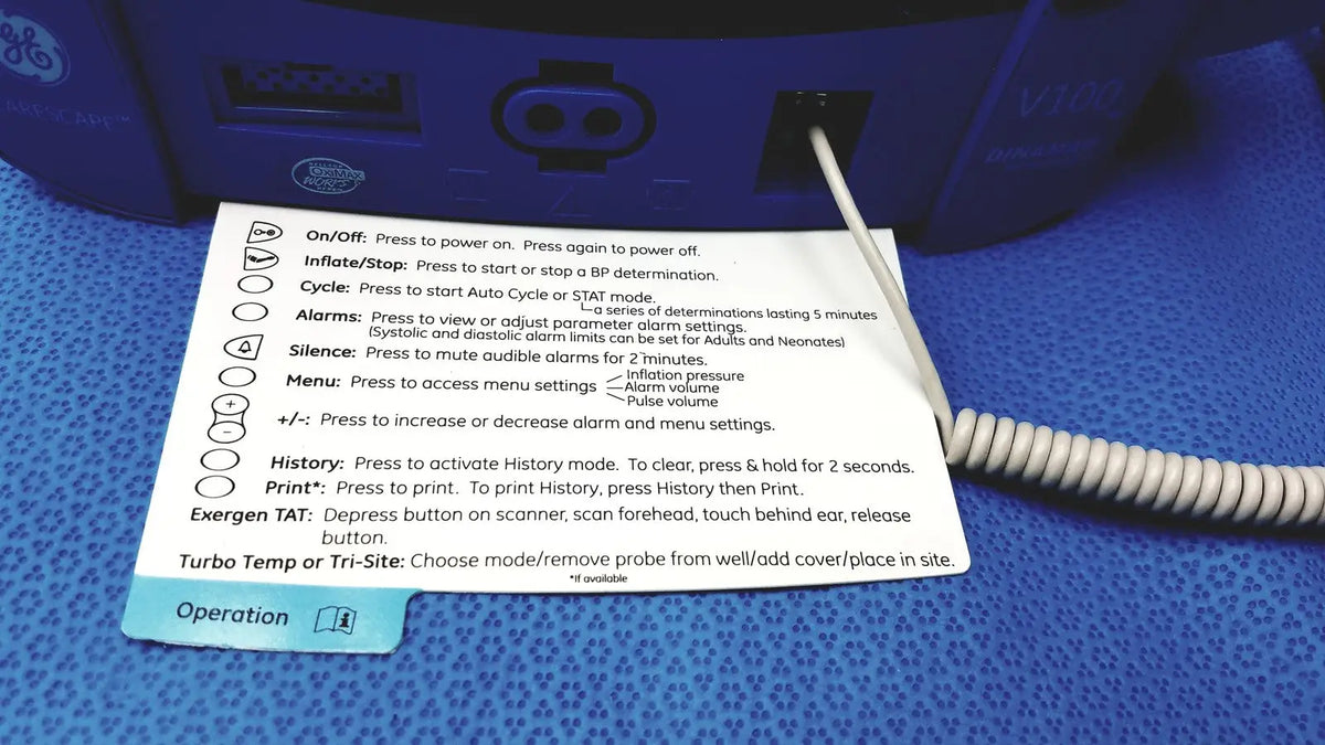 Blue ge carescape dinamap v100 vital signs monitor with white coiled cable and instruction card placed on surface