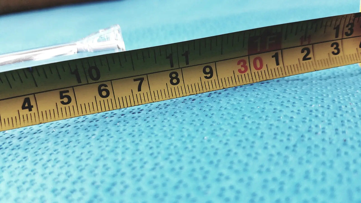 Yellow metal ruler with black and red markings on blue surface near a glass straight bore ground glass valve stopcock