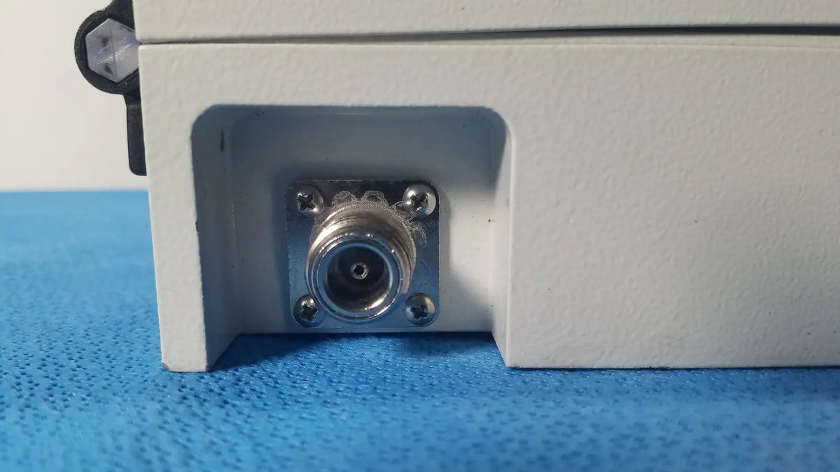 Silver n-type coaxial connector mounted on white plastic housing with screws on gms general microwave c/f-band receiver back side