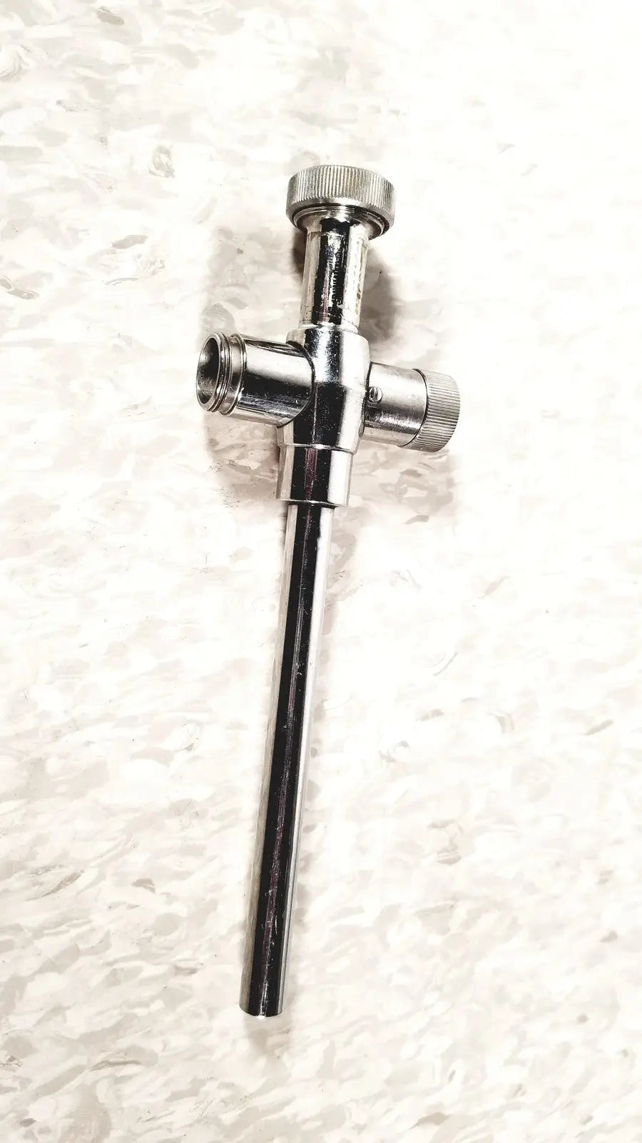 Shiny chrome-plated brass plumbing valve with cross-shaped body and threaded ends for reusable metal trocar sleeve use