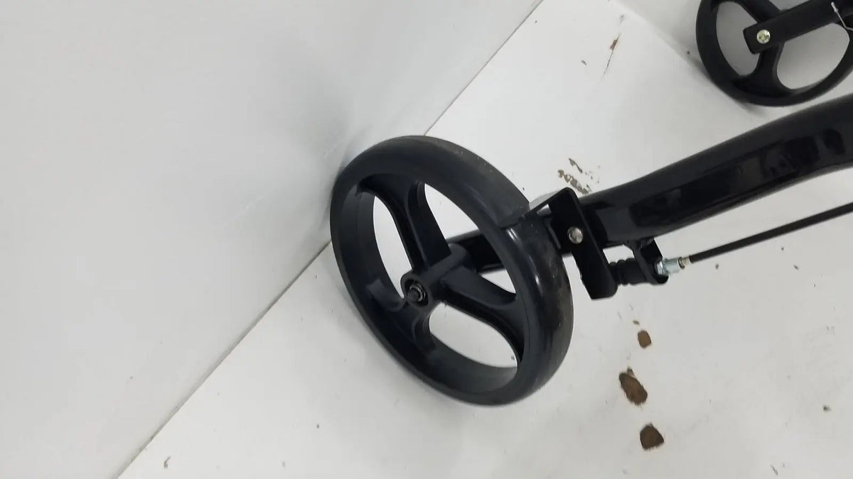 Black plastic wheel with three spokes attached to black metal frame of medline rolling walker mds8684gblkm with hand brakes