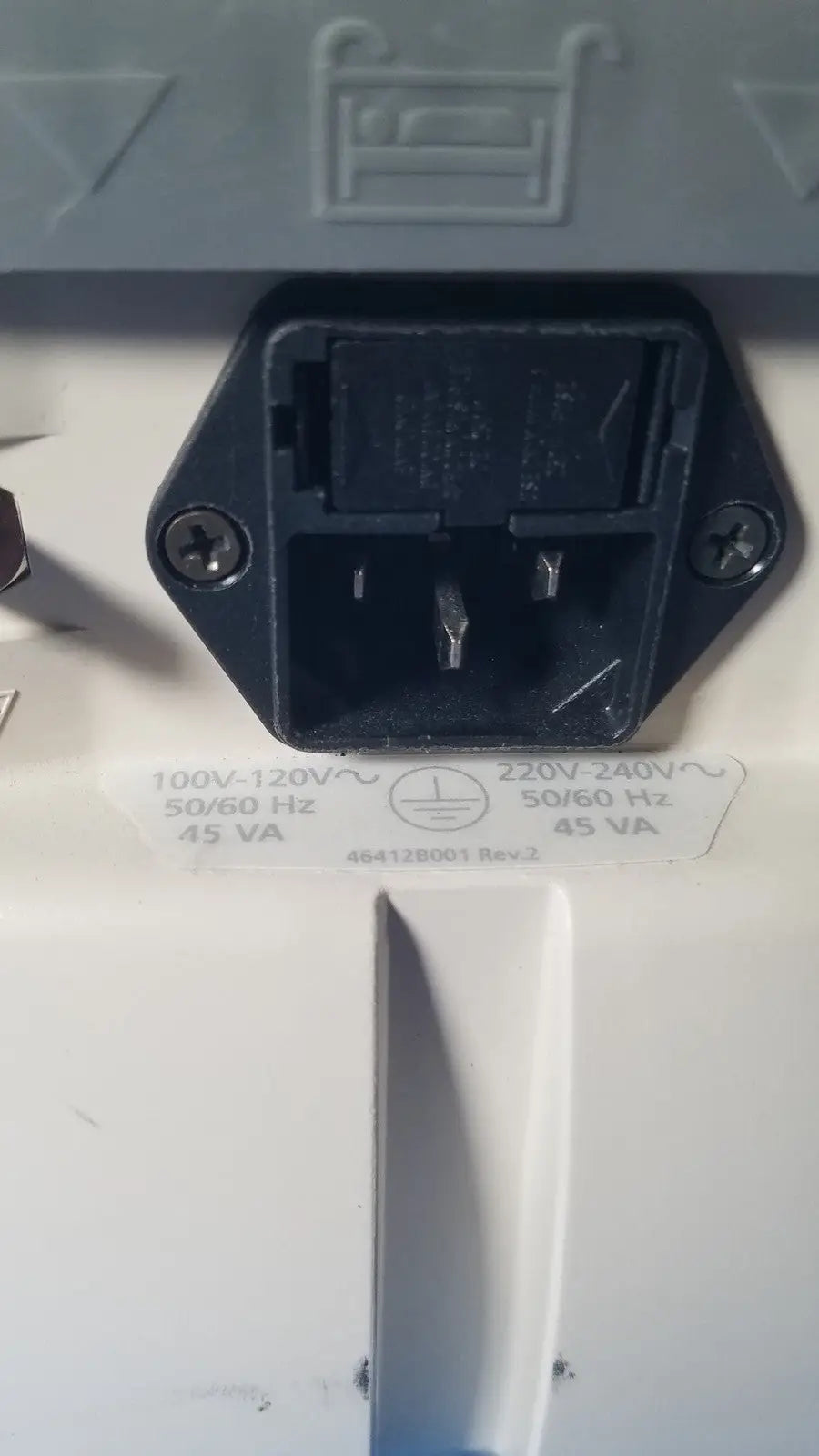 Black plastic electrical plug with two flat prongs and grounding pin on the back of a white medrad veris monitoring system casing