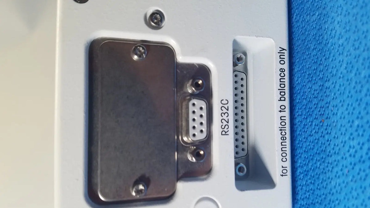 White plastic panel on the back of mettler toledo umx2 ultra-microbalance scale featuring metallic rs232c serial port and d-sub connector secured with screws