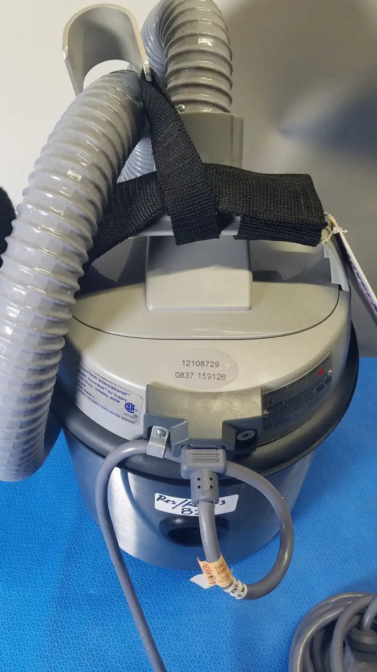Gray cylindrical nilfisk advance hovermatt air supply unit with flexible hoses and black strap securing attachments