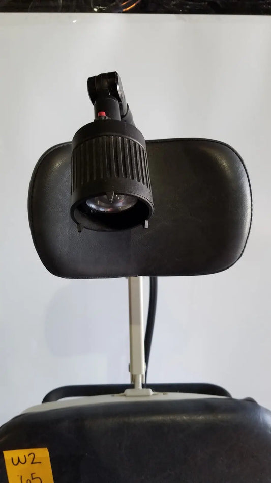 Black adjustable headrest-mounted lamp with ribbed housing and articulated arm on reliance medical products model 6100 exam chair