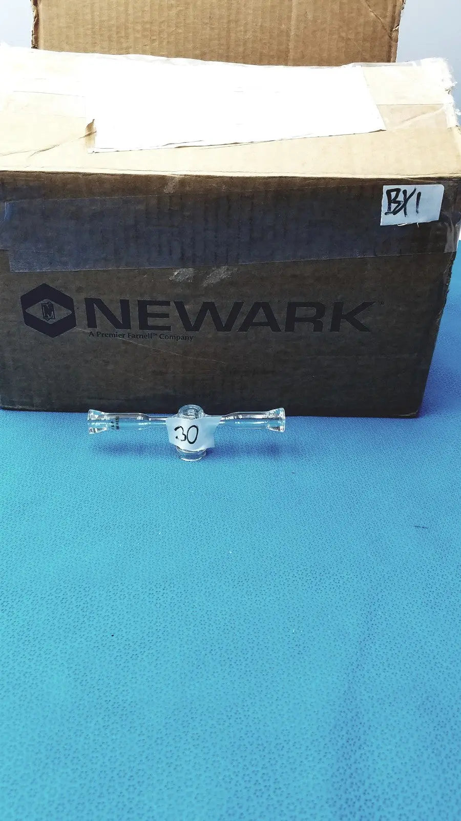 Clear borosilicate spherical joint glass stopcock valve with central 30 marking and flared ends on blue surface