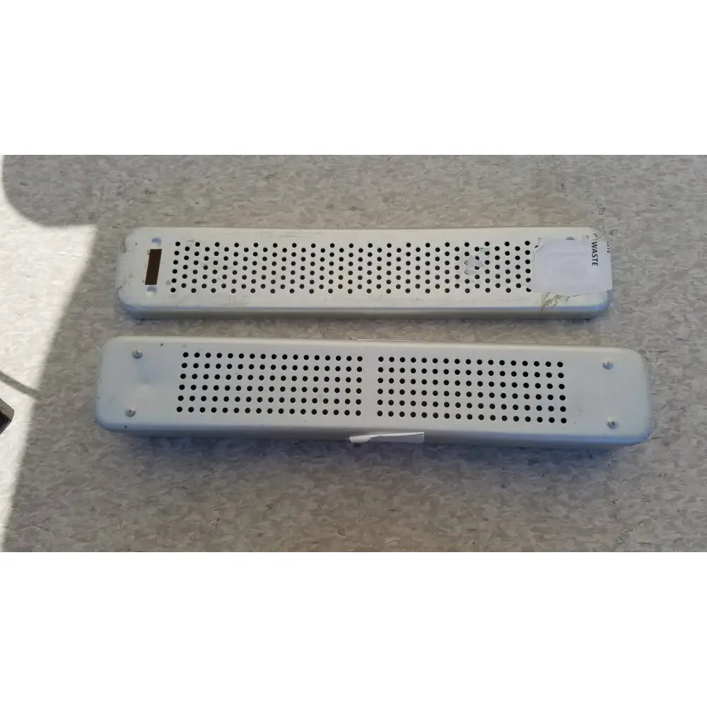 Two white plastic rectangular air vents with perforated surfaces and screws on steel healthcare equipment medical sterilization tray