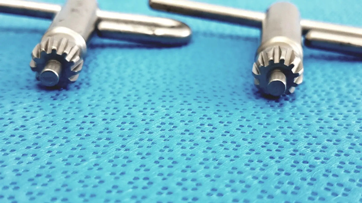 Silver stryker chuck key dental handpieces with gear-like tips resting on blue textured surface lot of 4 precision tools