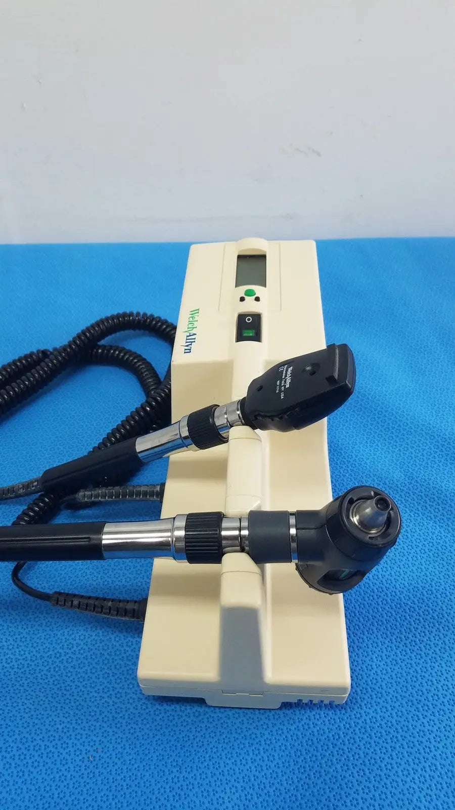 Beige hoya alpha ophthalmoscope with black and silver arms digital display and coiled cables in welch allyn series transformer for reuse medical use