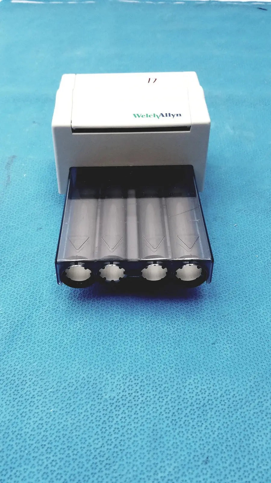White welch allyn universal battery charger with black tray holding four cylindrical batteries for universal kleenspec single use dispenser