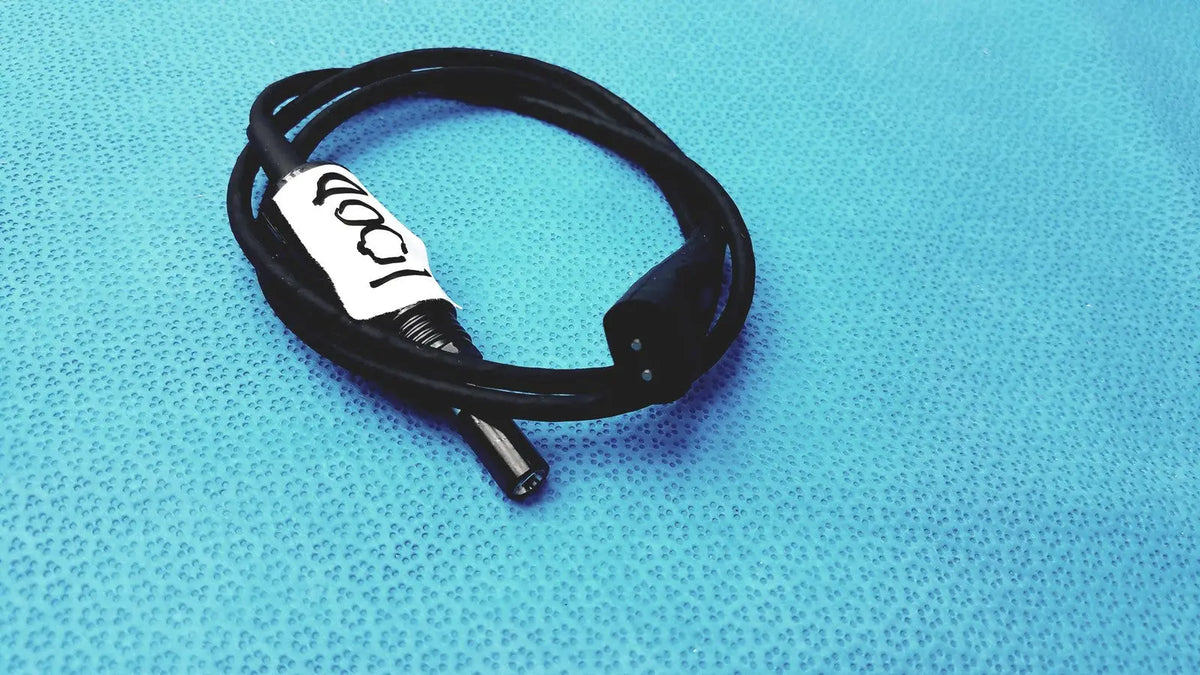 Black coiled 100cm smartwatch charging cable with safety protection features and two black connectors with white label 100