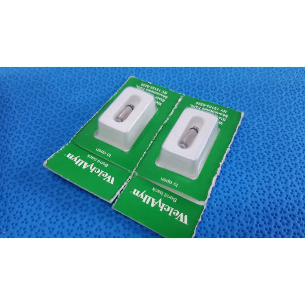 Two green cardboard packages each containing a white plastic encased stainless steel welch allyn allyn 04700-u replacement lamp bulb