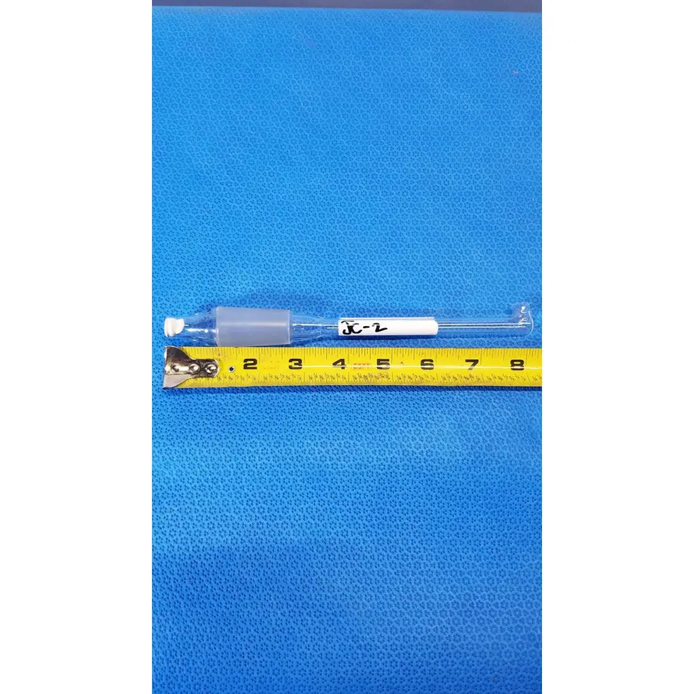 Clear glass thermometer adapter with gray plastic tip and white label xc-2 next to yellow measuring tape for lab thermometry use