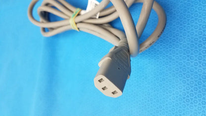 Gray 3-prong power cable coiled and secured by a yellow tie standard AC cord tested for reliability