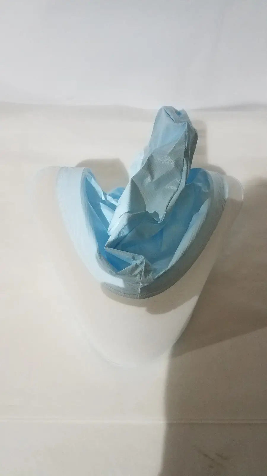 A crumpled light blue plastic be-12lb blue respirator headcover inside a white curved container for PAPR systems