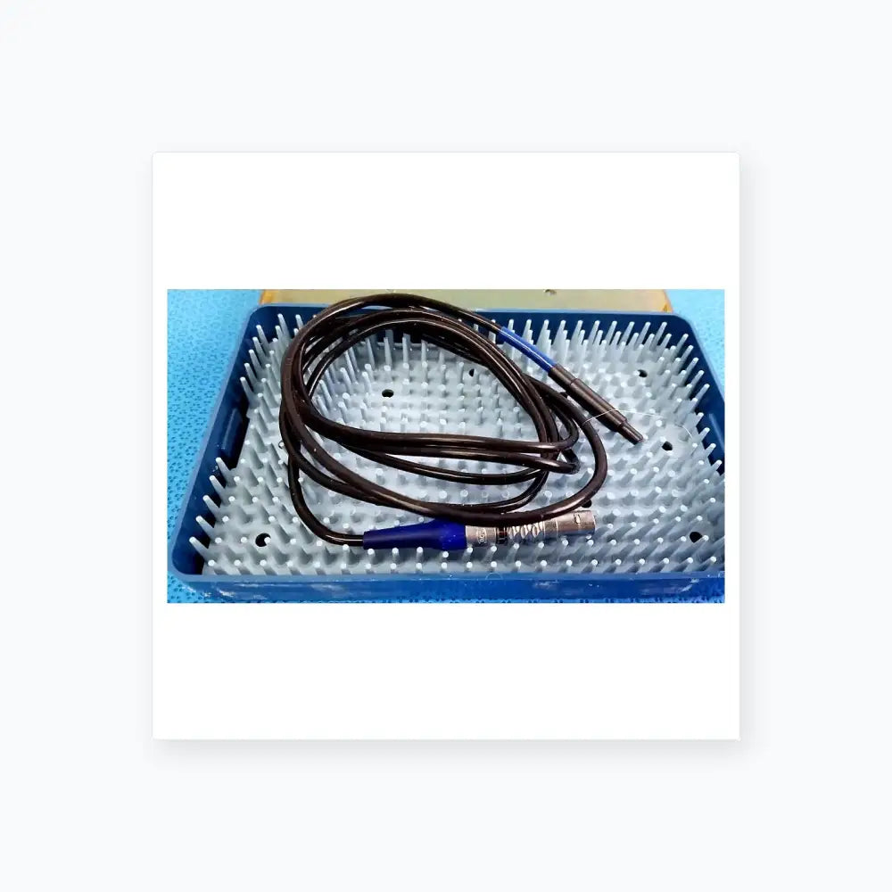 Black coiled cable with blue connectors and metallic end resting in blue sterilization tray for multigen radiofrequency probe