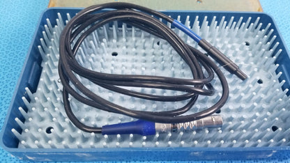 Black coiled cable with blue connectors and metallic end resting in blue sterilization tray for multigen radiofrequency probe