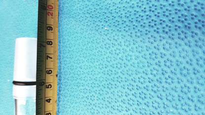 Ace glass thermometer adapter in white glass with black rubber band on neck next to yellow ruler on blue surface