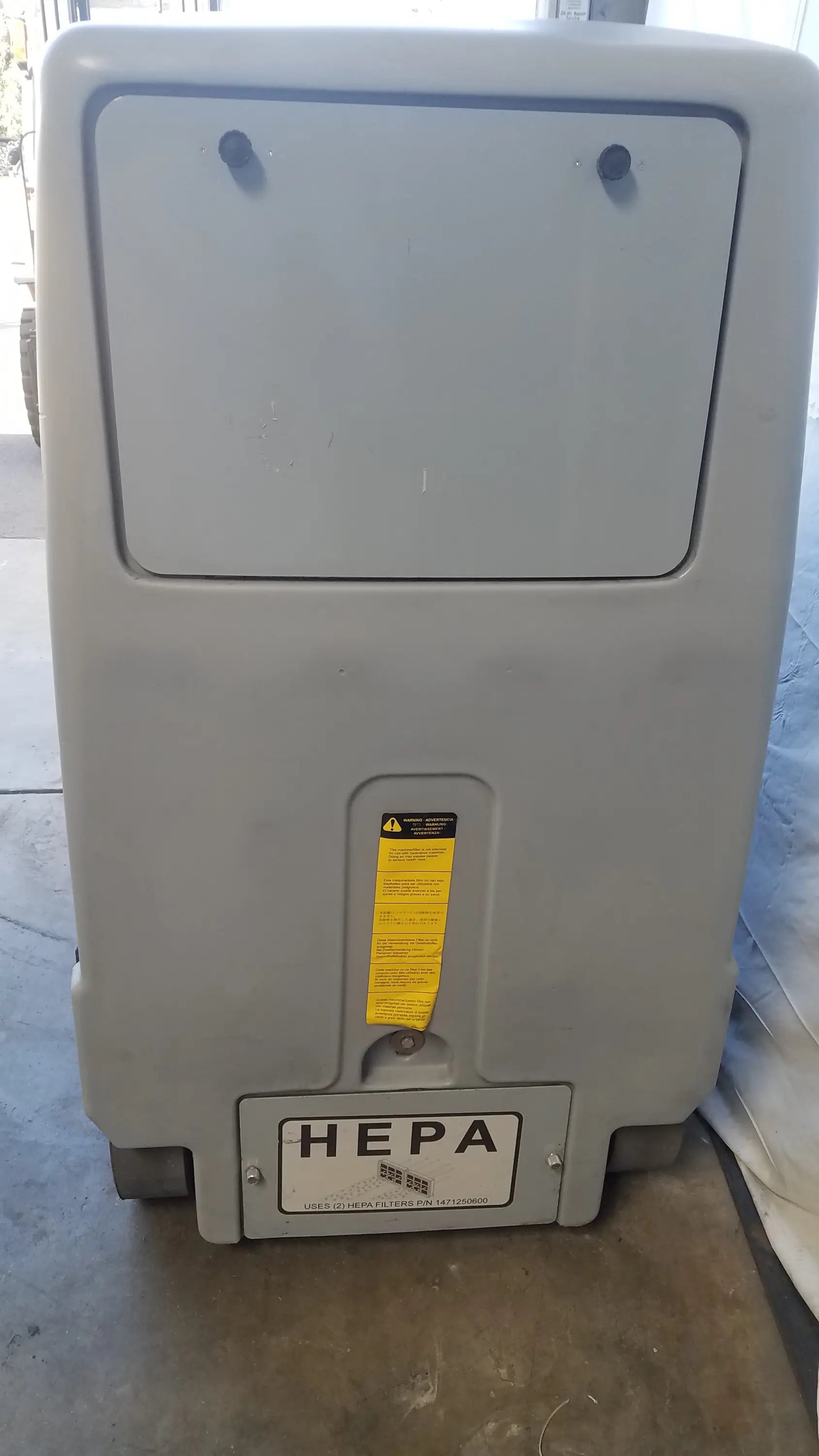 Gray plastic hepa filter unit with rectangular lid and warning label on advance ride on carpet cleaner extractor