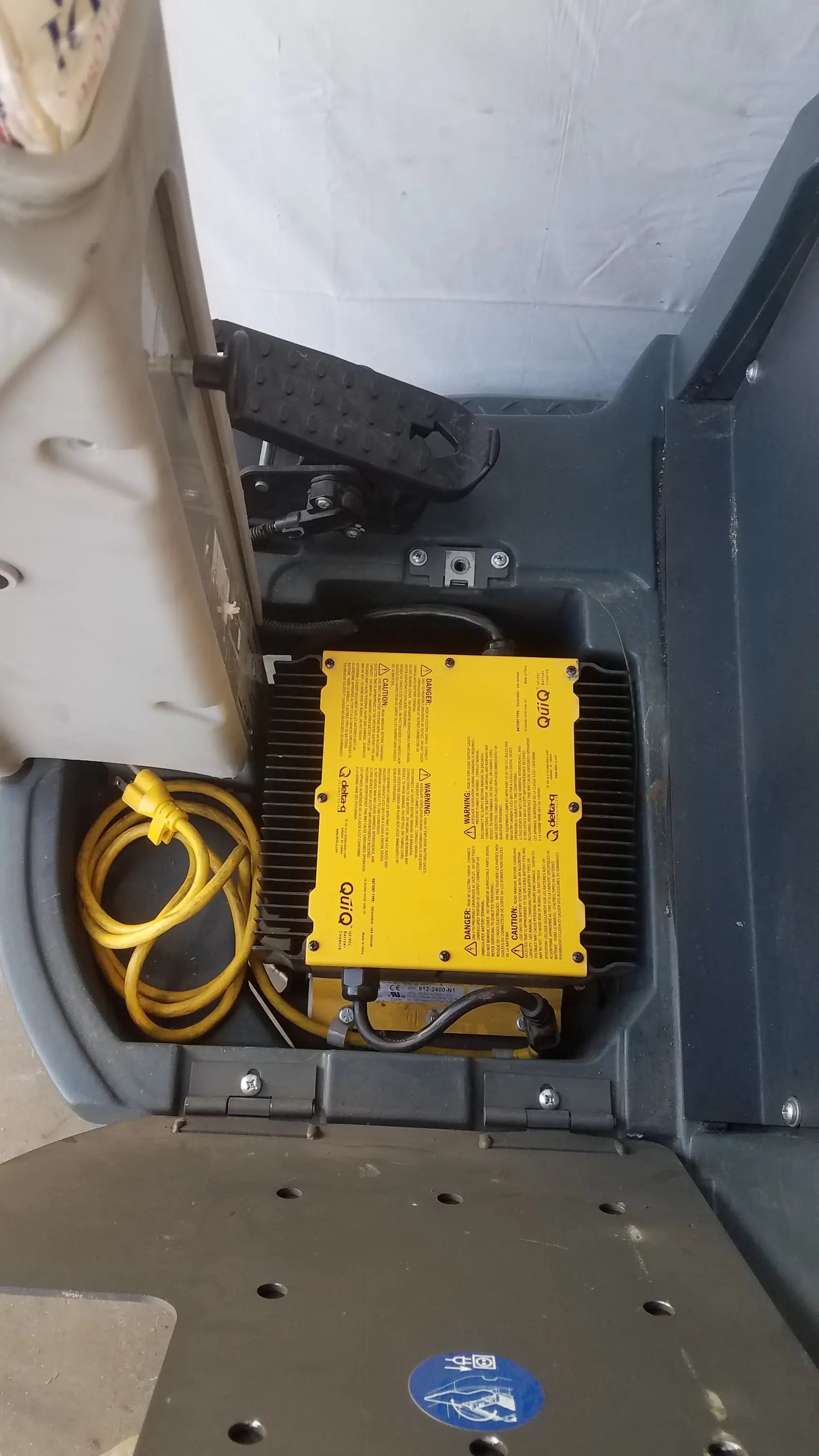 Yellow rectangular power inverter with black wiring and coiled yellow cord inside gray enclosure of advance ride on carpet cleaner extractor