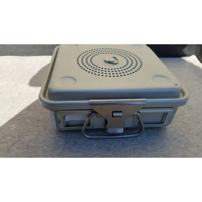 Gray plastic portable speaker with circular grille and metal handle shown alongside aesculap jk341 half size sterilization case