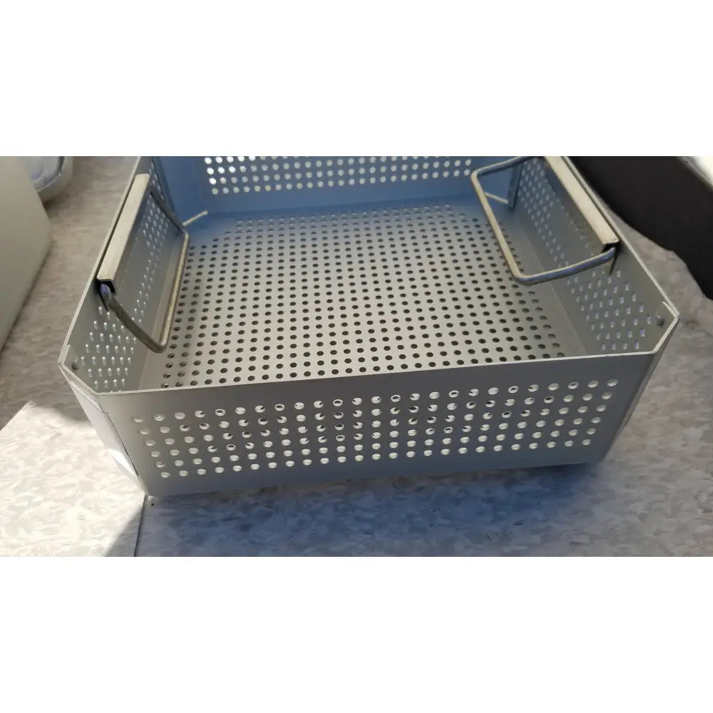 Gray perforated metal storage basket with reinforced side handles in aesculap jk341 half size sterilization case with lid
