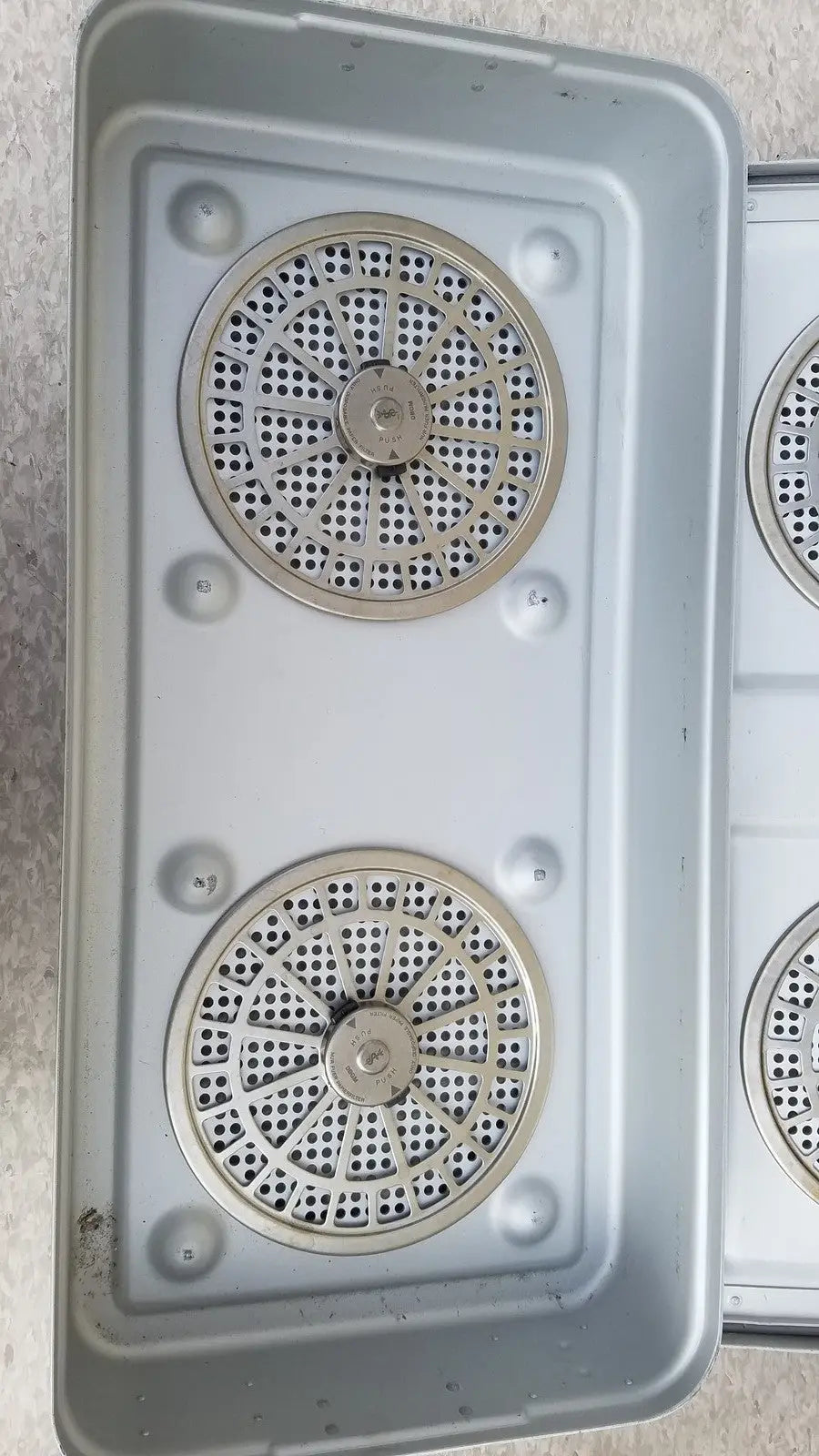 Silver metal grates with circular perforations and bolts inside an aesculap jn821 sterilization case instrument tray