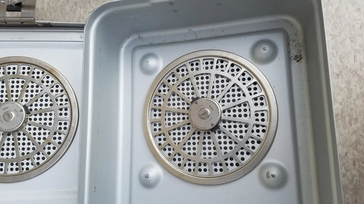 Silver metallic circular perforated grates set into a metal tray of the aesculap jn821 sterilization case instrument tray