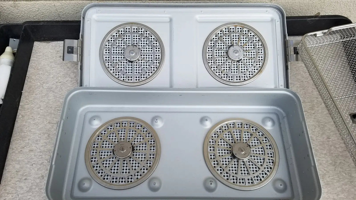 Silver-colored metal aesculap jn821 sterilization case instrument tray with four circular perforated heating elements in 2x2 grid