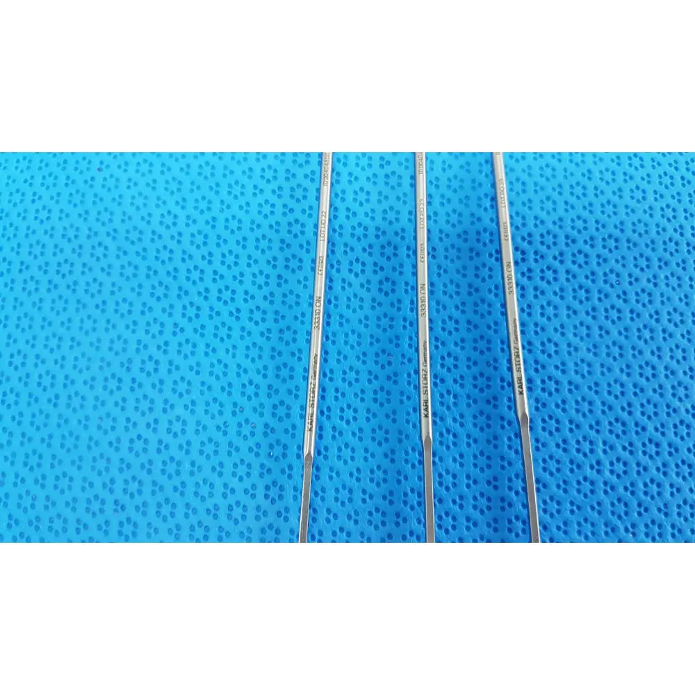 Three slender metallic aesculap laparoscopic instruments model 33310 with engraved markings on blue textured surface reuse medical