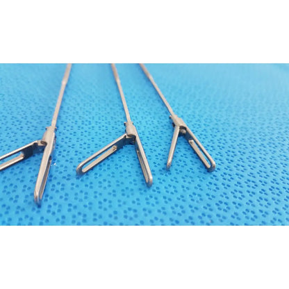 Three stainless steel aesculap laparoscopic instruments model 33310 with serrated jaws on blue textured surface