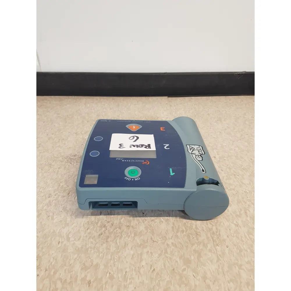 Blue-gray agilent heartstream fr2 semi automatic defibrillator with green power button and numbered front pads