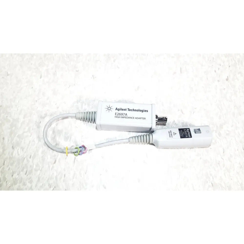 White agilent technologies e2697a high impedance adapter with gray coiled cables and a small black connector with papers