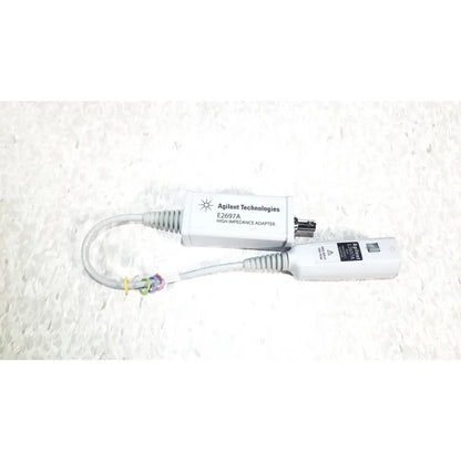 White agilent technologies e2697a high impedance adapter with gray coiled cables and a small black connector with papers