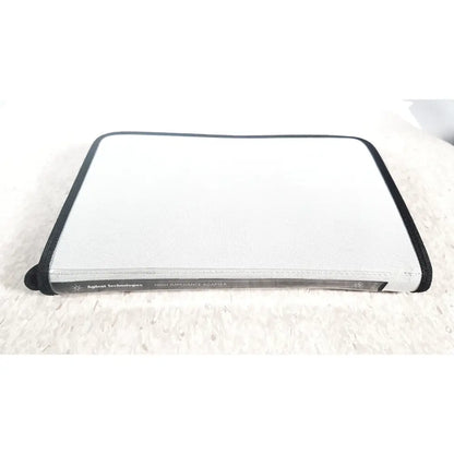 A sleek white and black agilent technologies e2697a high impedance adapter with a textured fabric exterior and papers