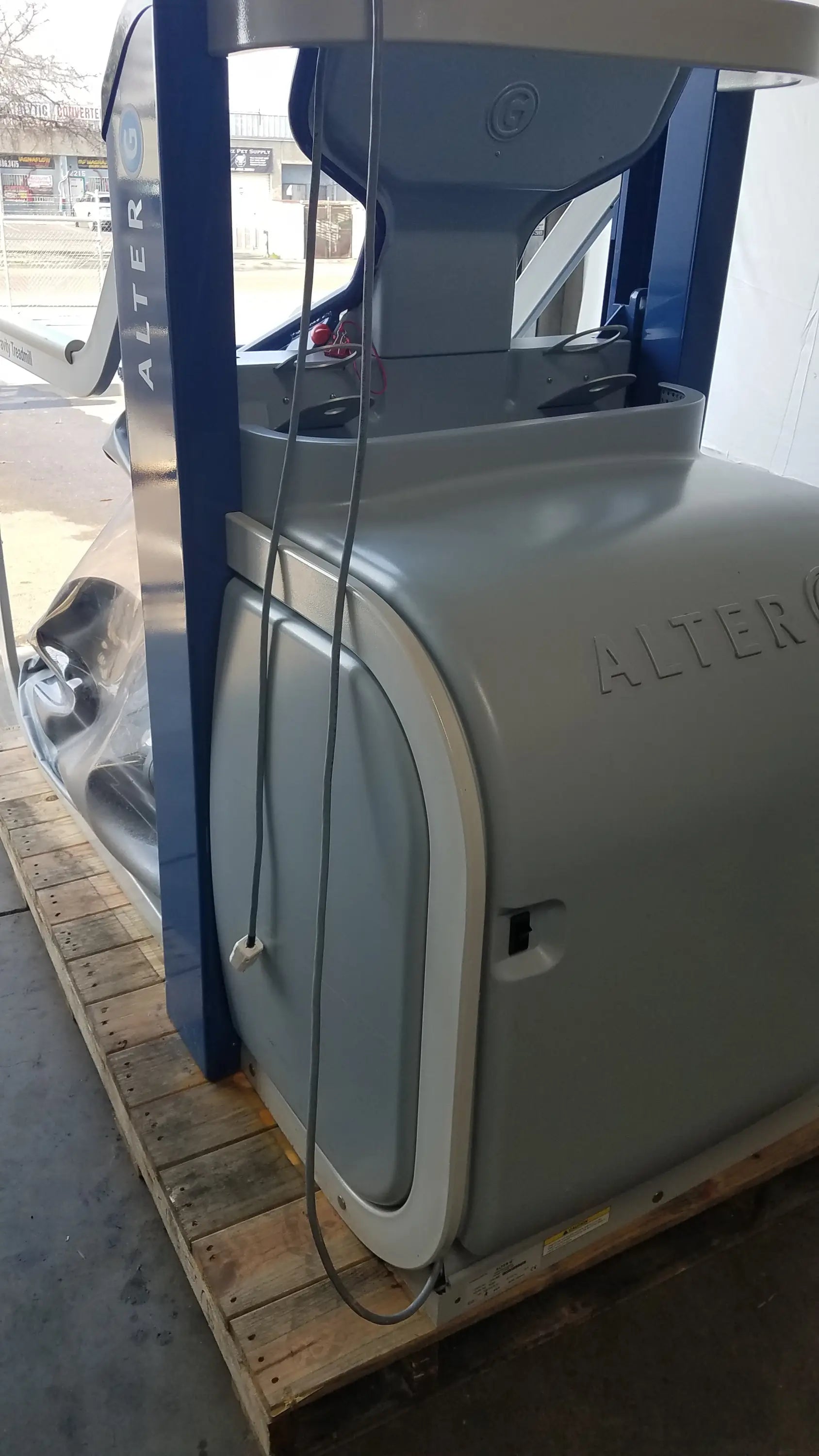 Gray and blue industrial forklift with alter branding beside an alter g m320 anti-gravity treadmill featuring adjustable body-weight support