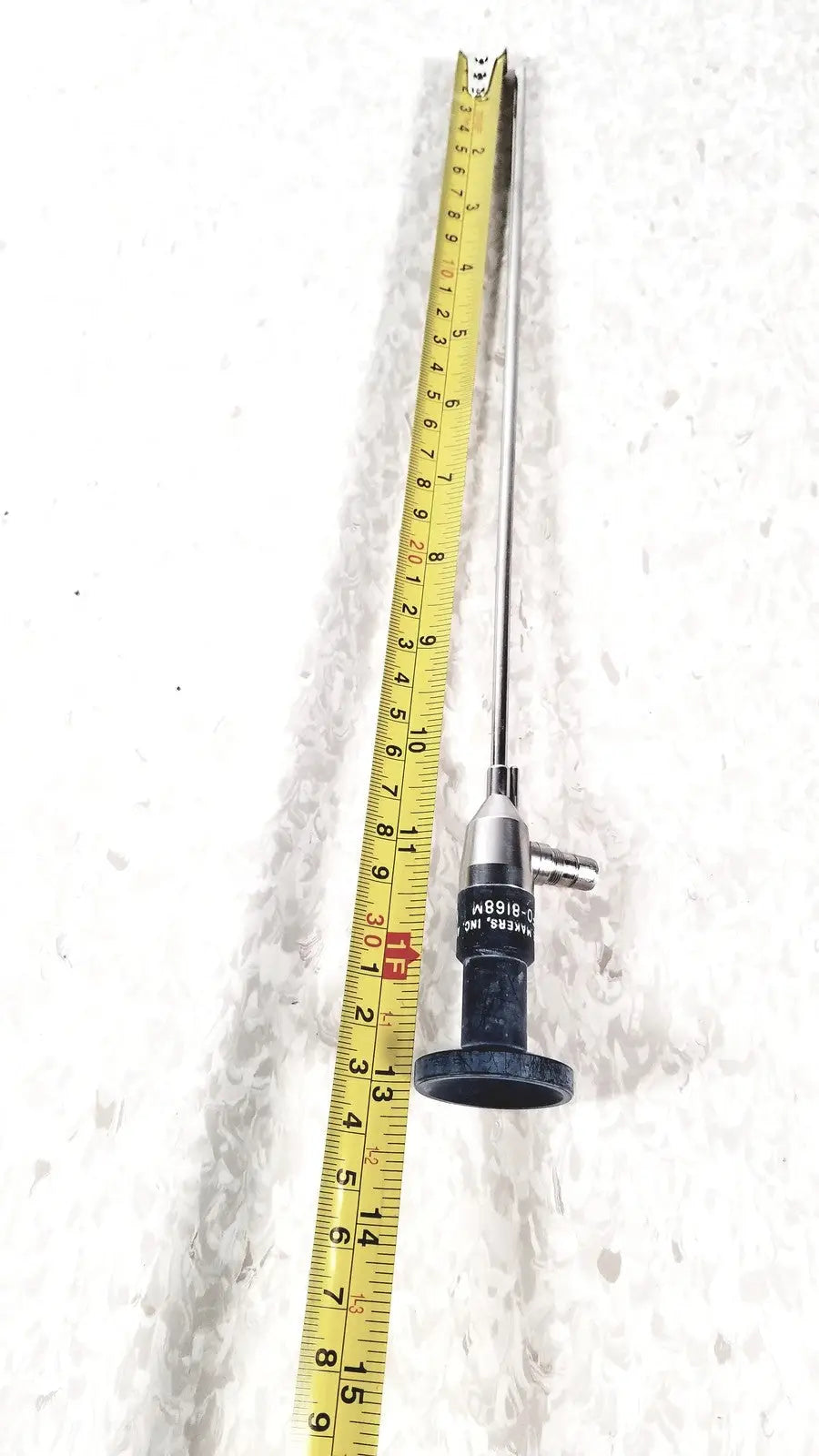 Silver surgical american cystoscope makers FO-8168M microlens with black handle and engraved markings beside yellow tape measure
