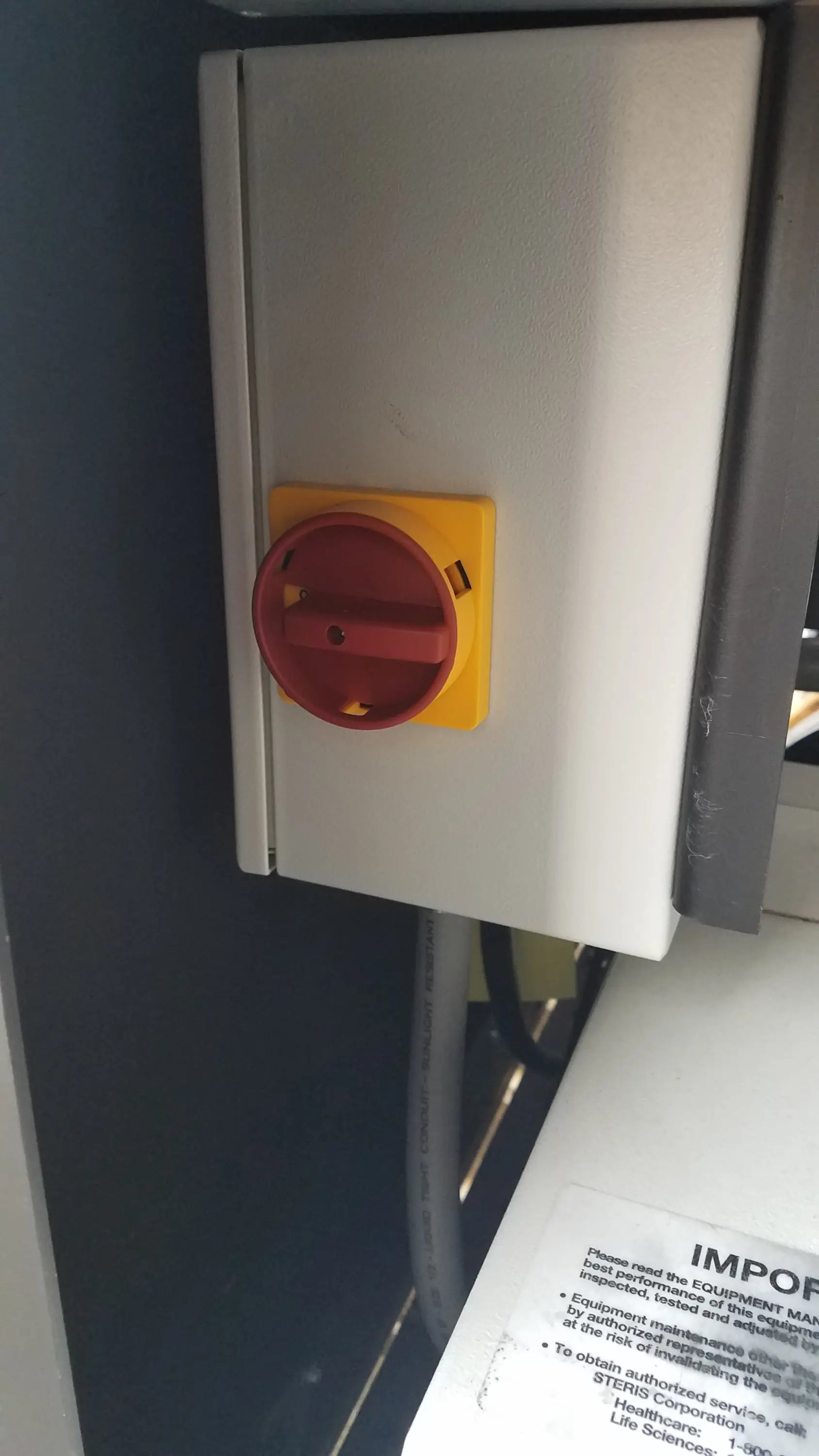A red emergency stop button on a yellow base in the gray metal enclosure of an amsco steris v-pro max low temperature sterilization system