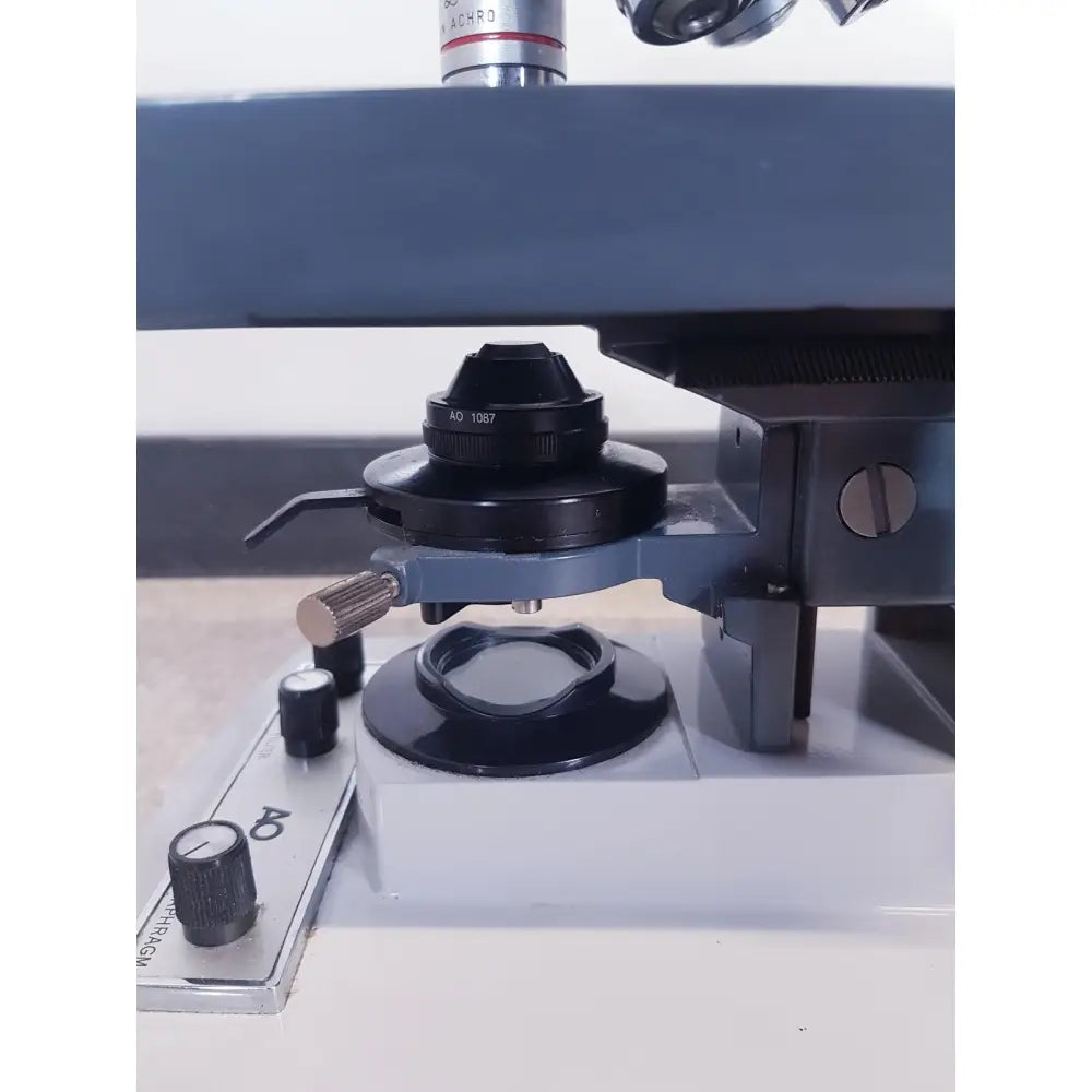 Black objective lens turret with silver adjustment knobs on gray base of ao scientific instruments one-ten illuminator model 1130a