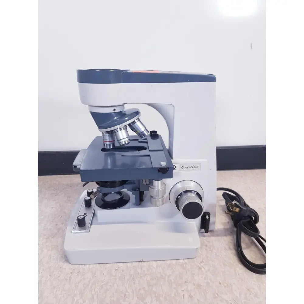 Gray and white compound microscope with metallic lenses and labeled one-ten illuminator model by AO Scientific Instruments